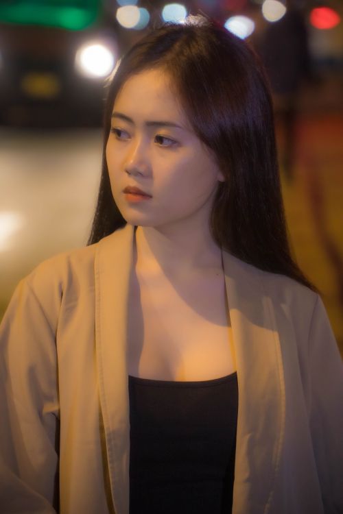 Free Young woman in a city street at night, illuminated by warm street lights, looking thoughtfully. Stock Photo