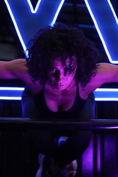 Woman focusing on intense workout under dramatic neon lights for fitness inspiration.