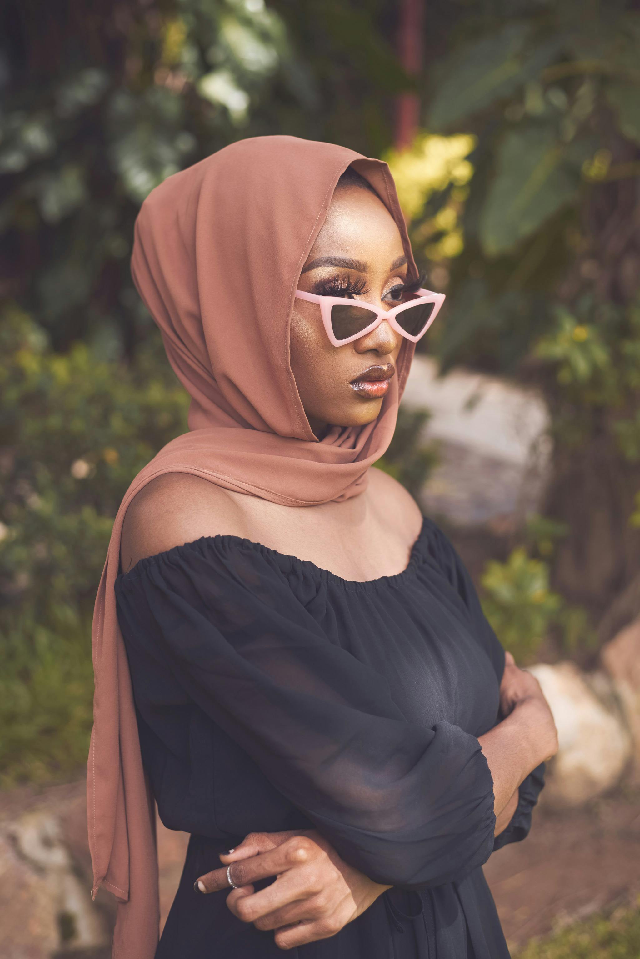 Stylish young woman wearing a hijab and sunglasses posing outdoors with a modern fashion vibe.