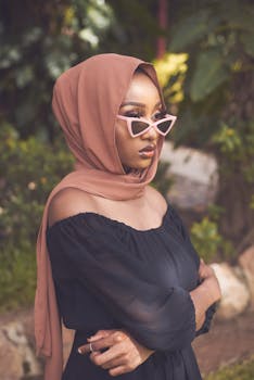 Stylish young woman wearing a hijab and sunglasses posing outdoors with a modern fashion vibe.