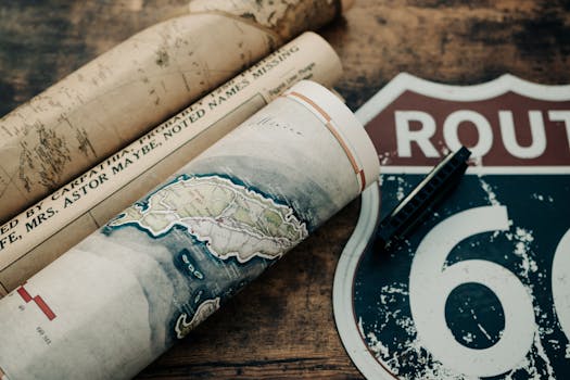 Close-up of rolled vintage maps and Route 66 sign on wooden surface, capturing nostalgia and exploration.