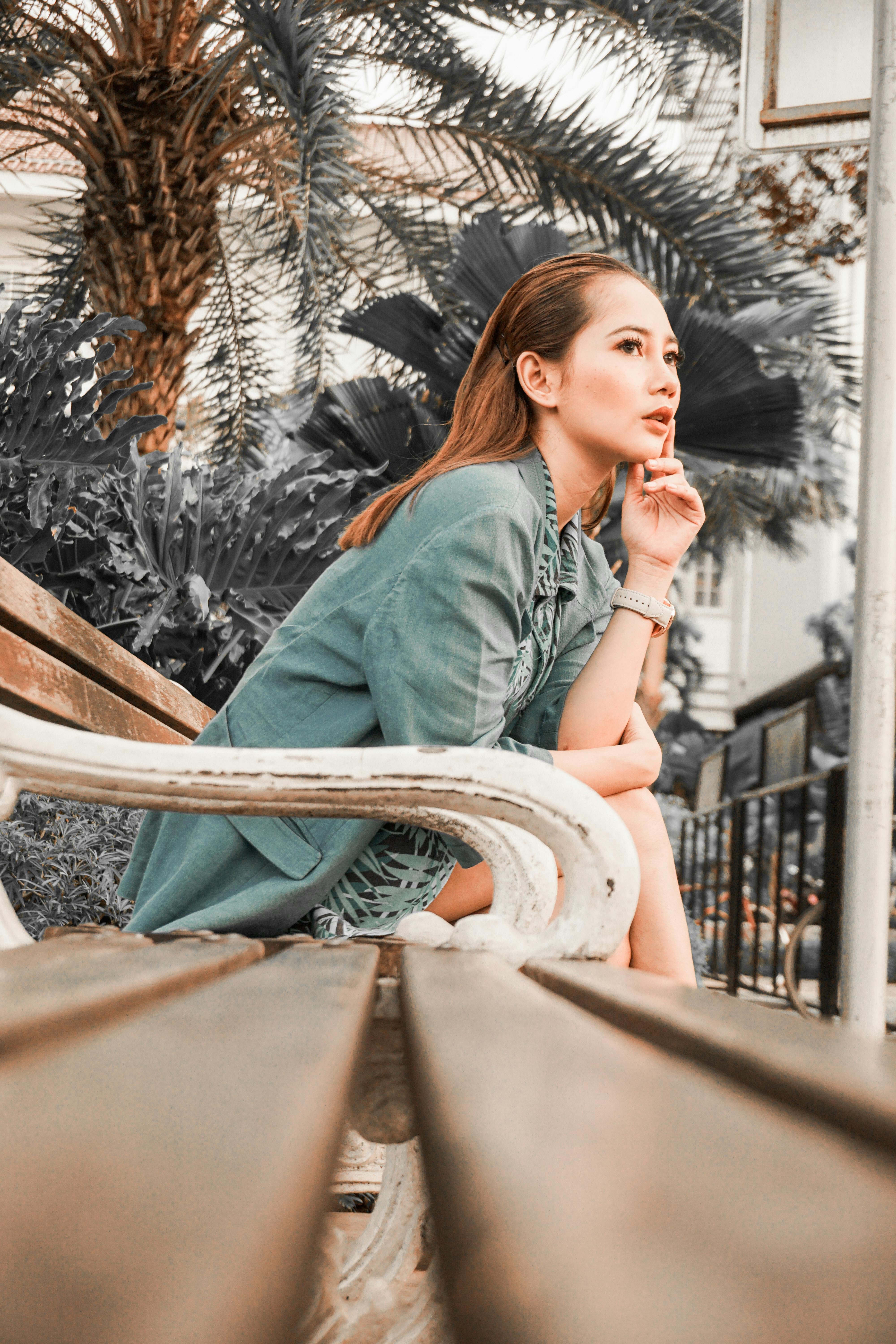 Side view of a fashionable woman sitting thoughtfully on a bench in an outdoor setting.