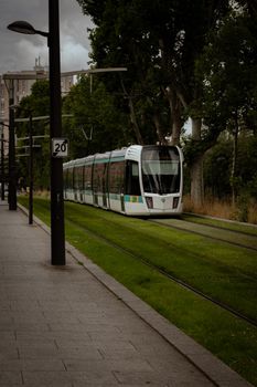 A modern tram travels on lush green tracks through a serene urban setting in Paris, France.