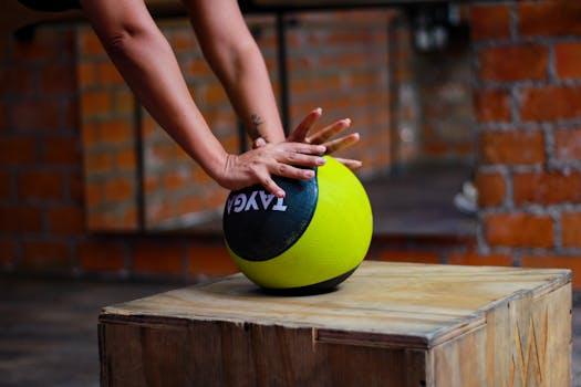 Close-up view of hands using a medicine ball on a wooden box in a gym, ideal for fitness themes.