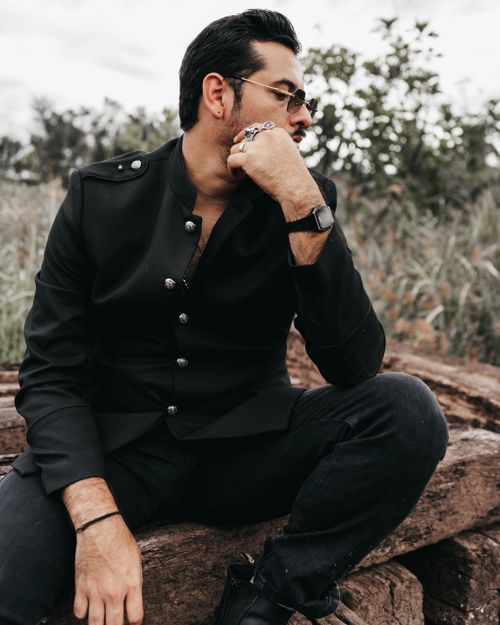 Free Portrait of a stylish man in sunglasses sitting on a log outdoors. Stock Photo