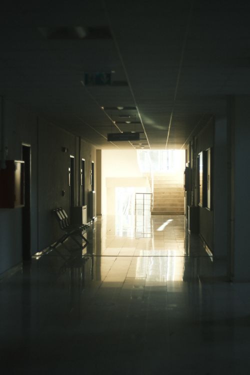Free A dimly lit corridor with reflections on the floor leading to a brightly illuminated staircase. Stock Photo