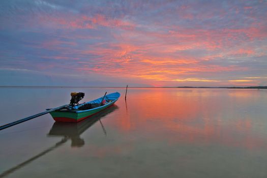 平静的海面上，一艘孤船倒映着绚烂天空的宁静日落