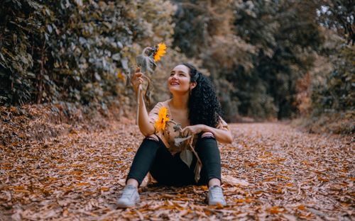 Free Smiling woman holding sunflowers on a leaf-covered path in fall. Stock Photo