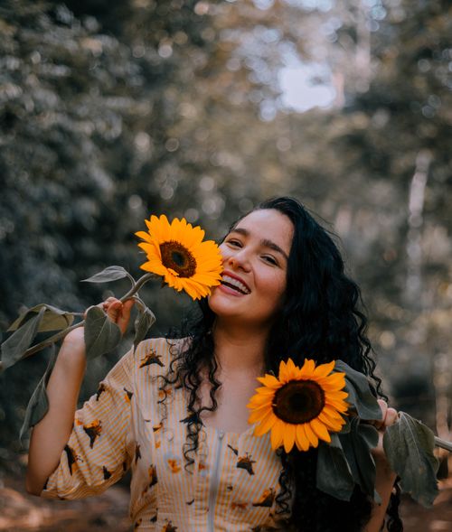 Free A joyful woman with curly hair holding vibrant sunflowers in a lush outdoor setting. Stock Photo