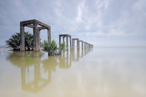 Gray Concrete Arches on Body of Water Under White Skies