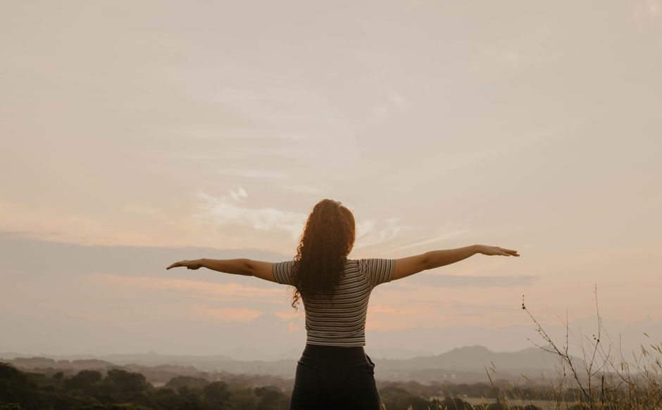 Woman standing with open arms at a beautiful sunset over rolling hills