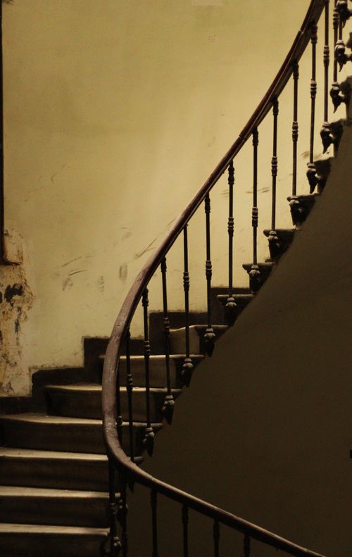 Free Vintage interior staircase with ornate iron handrail in low light, emphasizing architectural design. Stock Photo