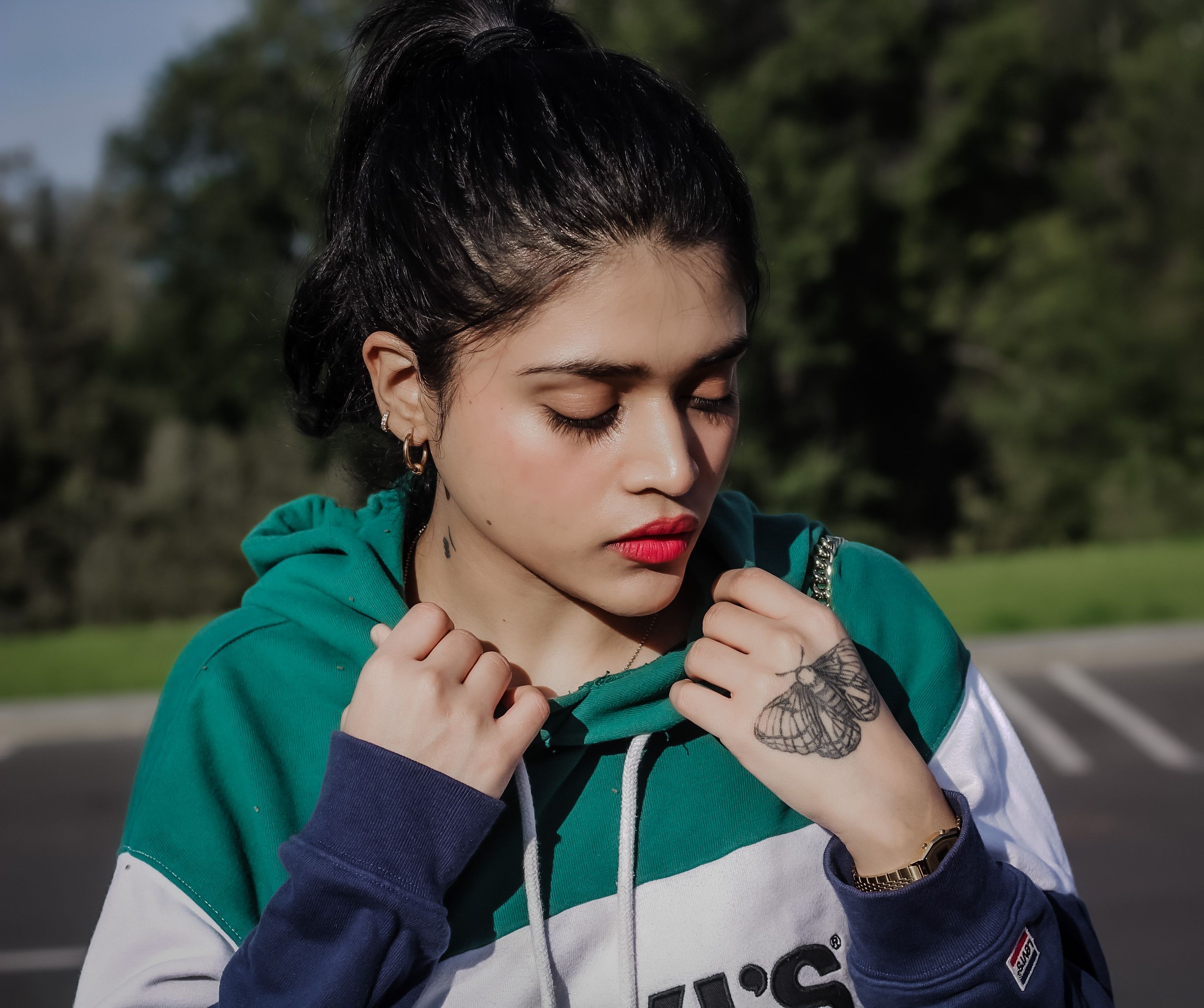Close-up portrait of a woman wearing a hoodie outdoors in Moldova, showcasing a butterfly hand tattoo.
