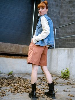 A stylish woman poses outdoors in an urban setting, wearing modern fall fashion.