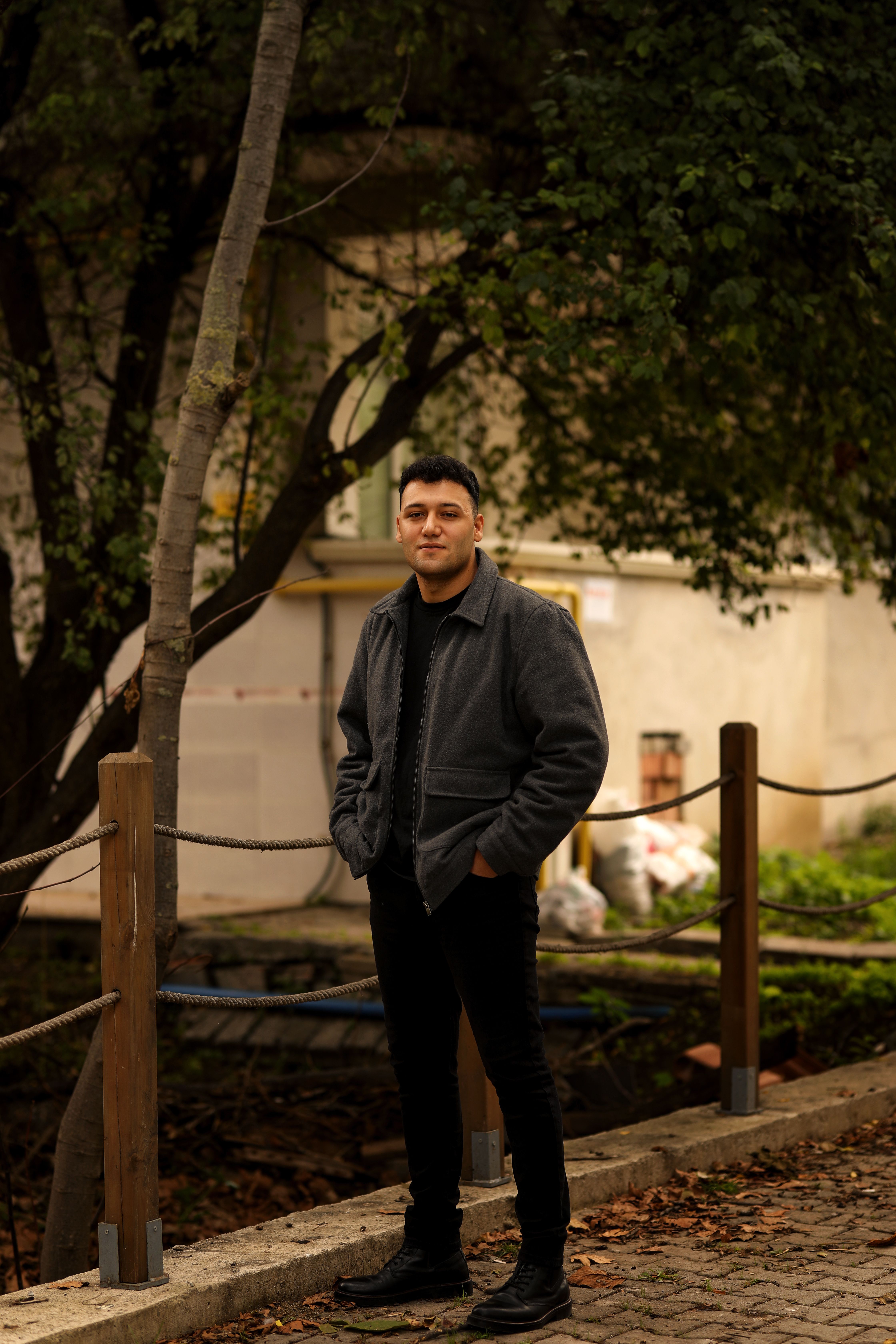 A man in a jacket stands outdoors on a path in Samsun, Turkey, amid lush greenery.