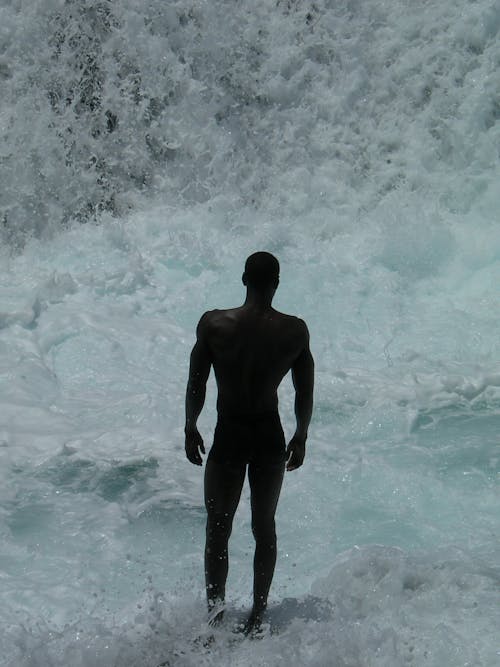Back View of a Shirtless Man Near a Waterfall