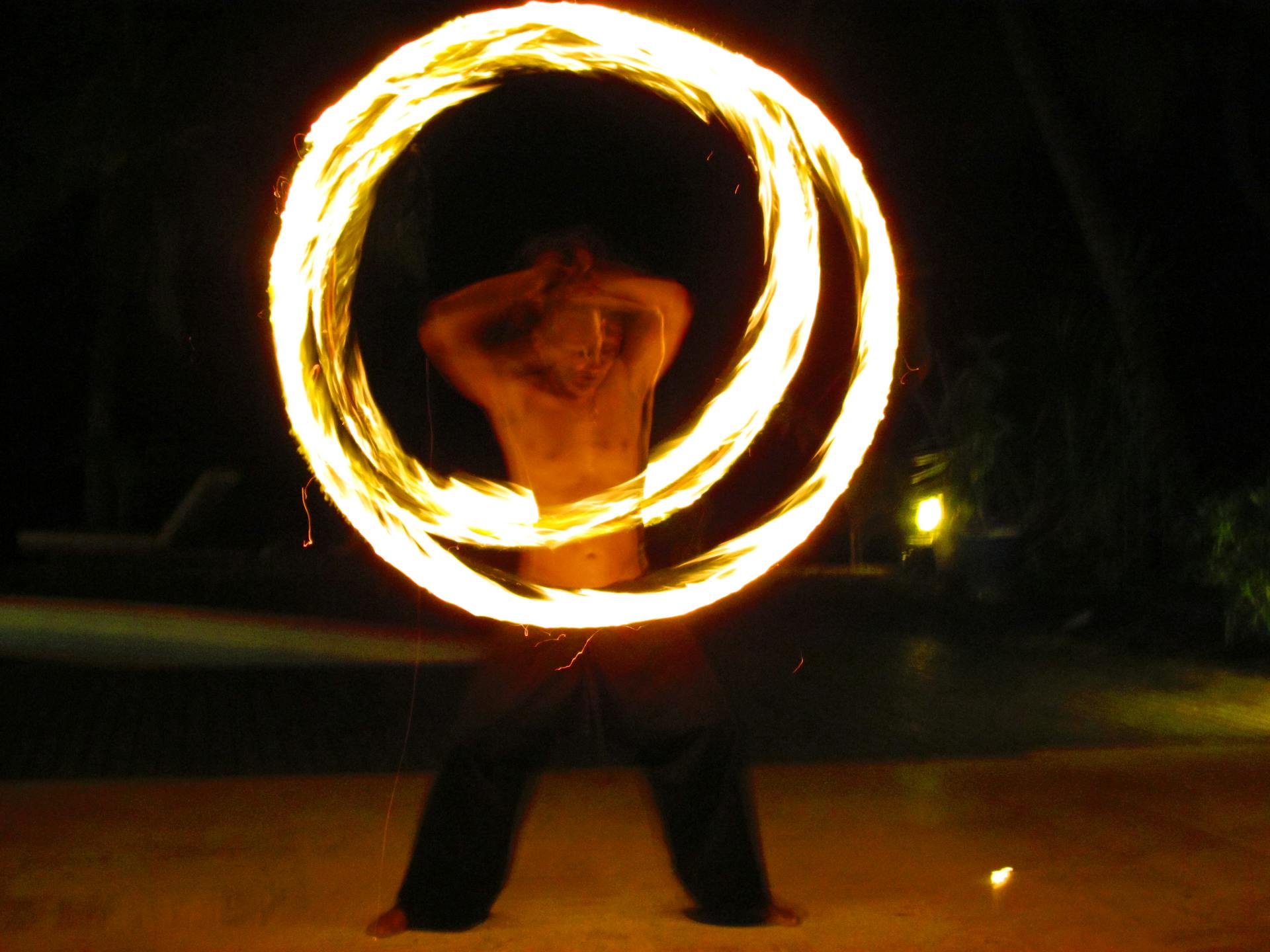 Shirtless performer creates dynamic spirals of fire against a night sky.