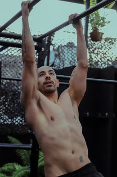 A fit man performs pull-ups on a bar, showcasing strength and fitness outdoors.