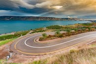 在戏剧性的天空下，弯曲的道路旁可见宁静的蓝色湖泊，四周环绕着郁郁葱葱的乡村