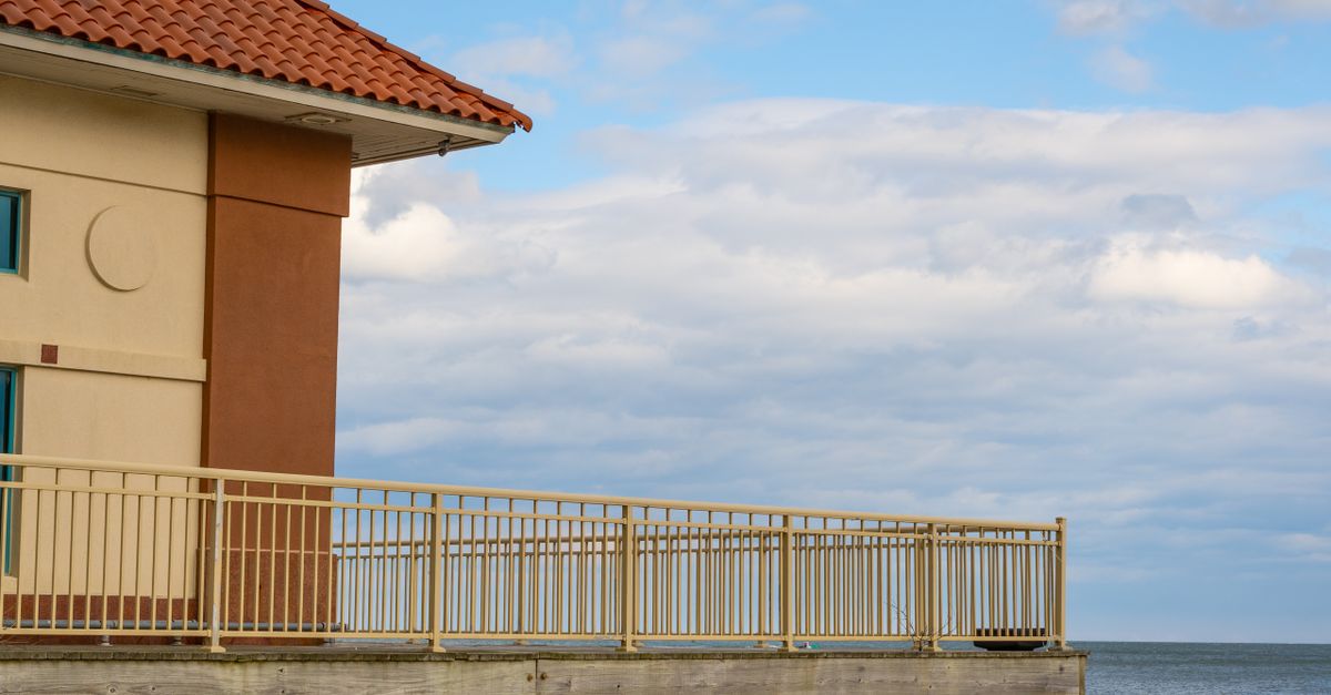 A scenic view from a seaside balcony overlooking the ocean under a partly cloudy sky.