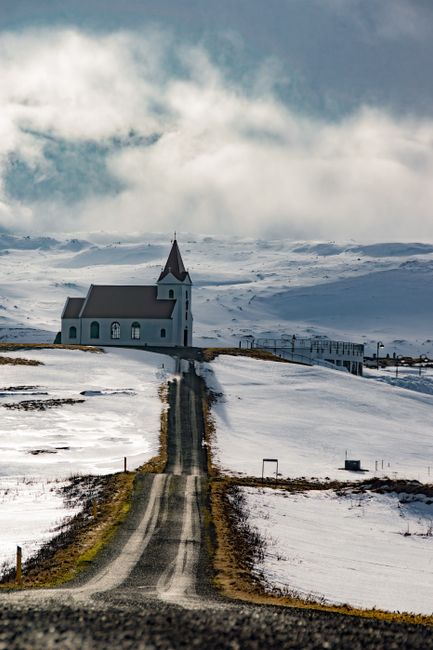 An isolated church amidst a snowy Icelandic landscape under a cloudy sky.