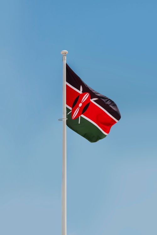 Free A vertical shot of the Kenyan national flag fluttering against a clear blue sky, symbolizing pride and patriotism. Stock Photo