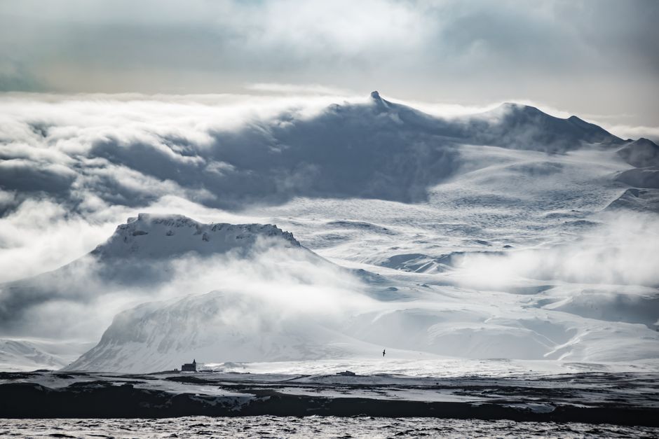 Breathtaking view of snowy mountains in Iceland enveloped by fog and dramatic clouds.