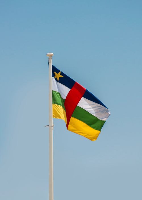 Free Central African Republic flag fluttering on a flagpole against a bright blue sky, signifying patriotism. Stock Photo