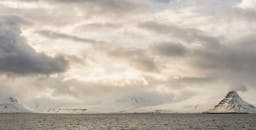 在戏剧性的云层下，冰岛柯克朱菲尔山与海浪构成了迷人的冬季场景