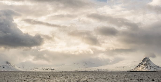 在戏剧性的云层下，冰岛柯克朱菲尔山与海浪构成了迷人的冬季场景