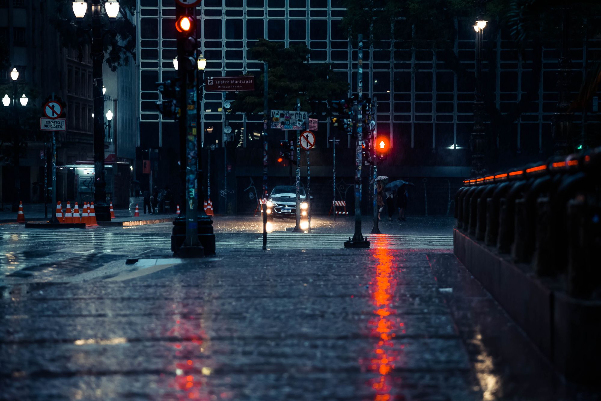 Urban street scene with wet crosswalk and traffic lights during a rainy night.