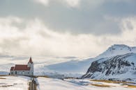 在白雪皑皑、群山密布的冬日，一座风景如画的教堂矗立在多云的天空下