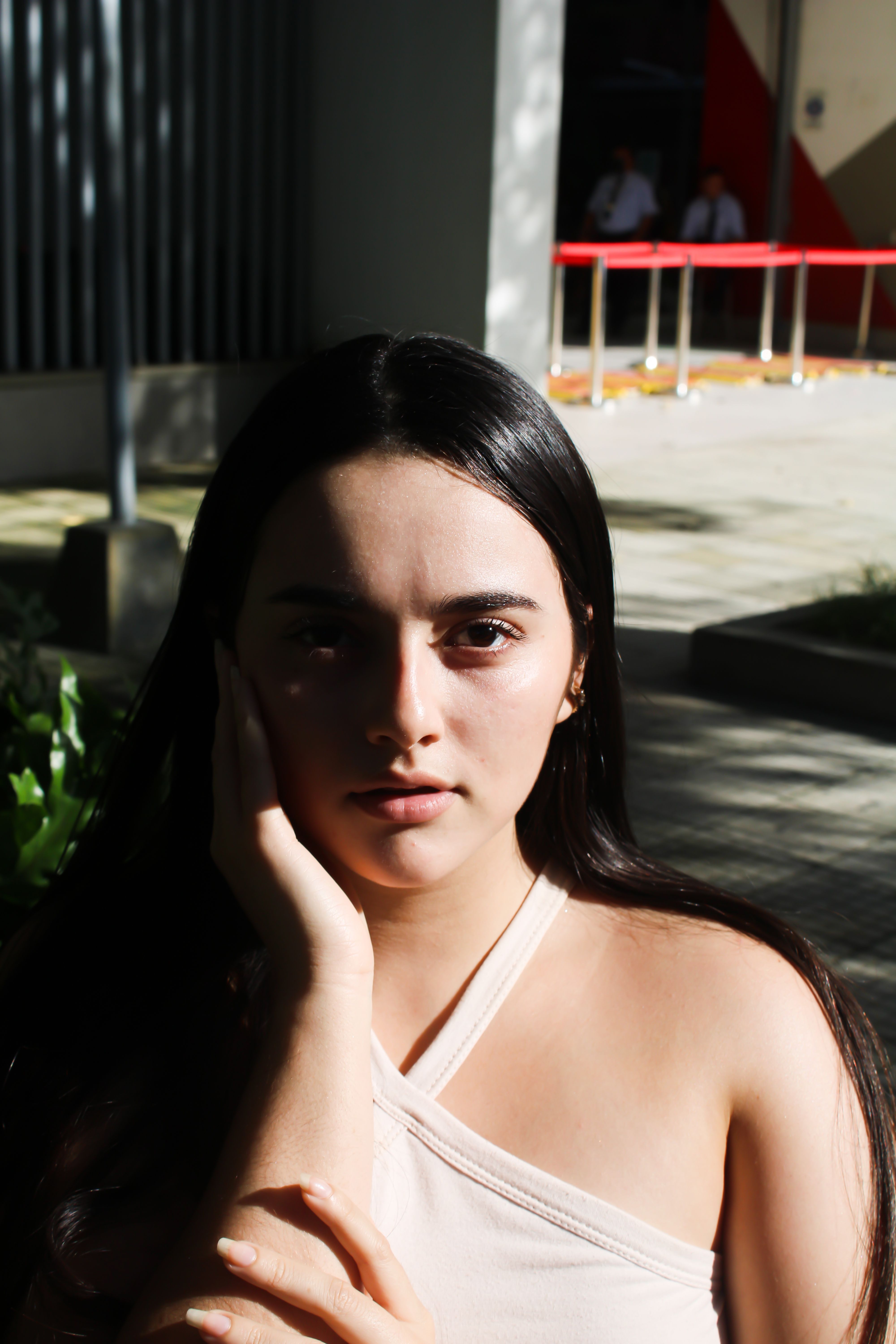 Elegant portrait of a woman with dark hair, hand resting on face, outdoors under sunlight.