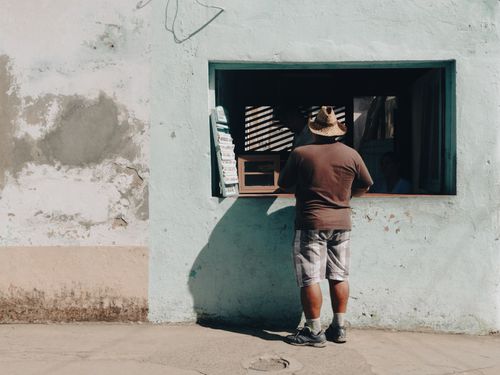 Free Man in casual attire at an outdoor retail window, standing in sunlight. Stock Photo