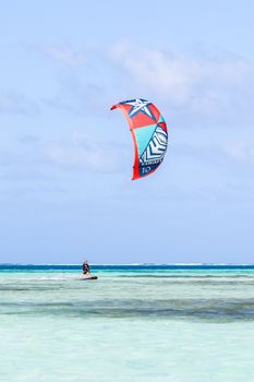Kiteboarding enthusiast gliding over turquoise sea under a clear blue sky, enjoying a summer water sport adventure.