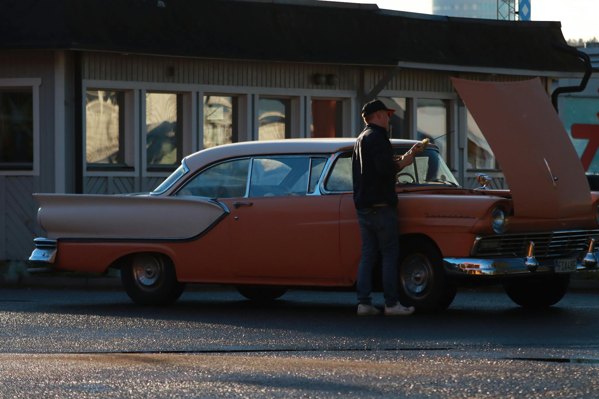 A man inspects a vintage car with the hood open on a street in Jönköping, Sweden.