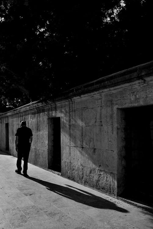 Grayscale Photo of Man Walking Along a Wall