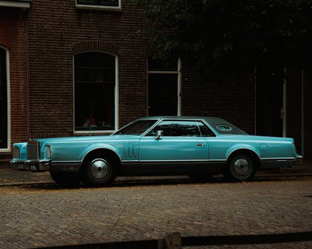 Classic blue car parked on cobblestone street in urban setting.