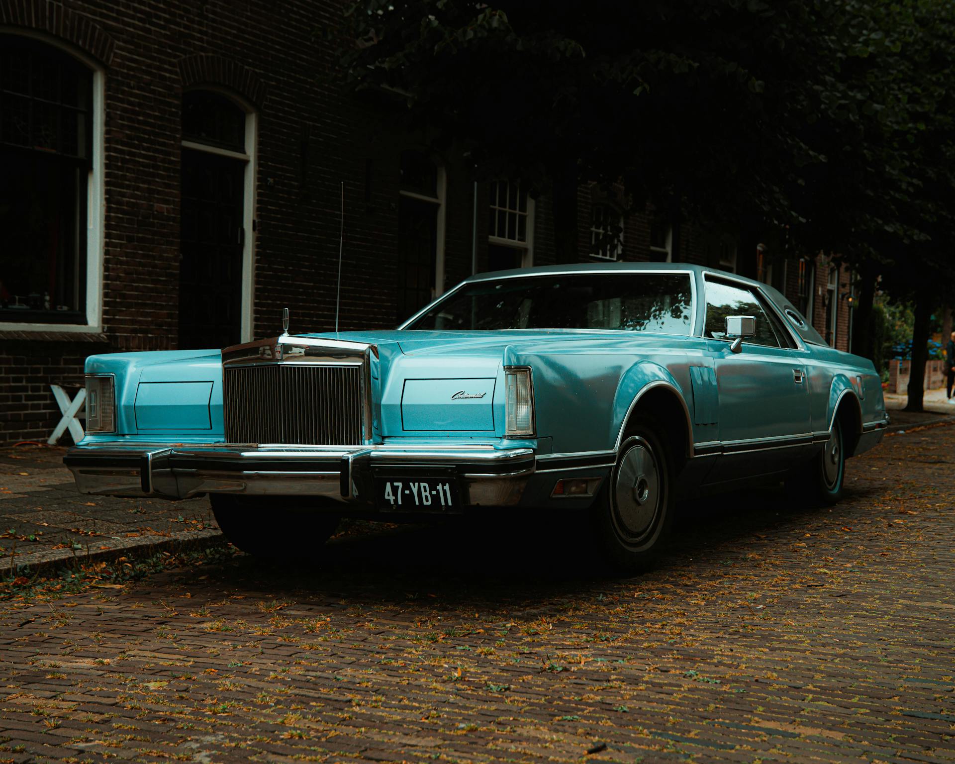 Classic blue Lincoln Continental Mark V parked on urban street with brick road.