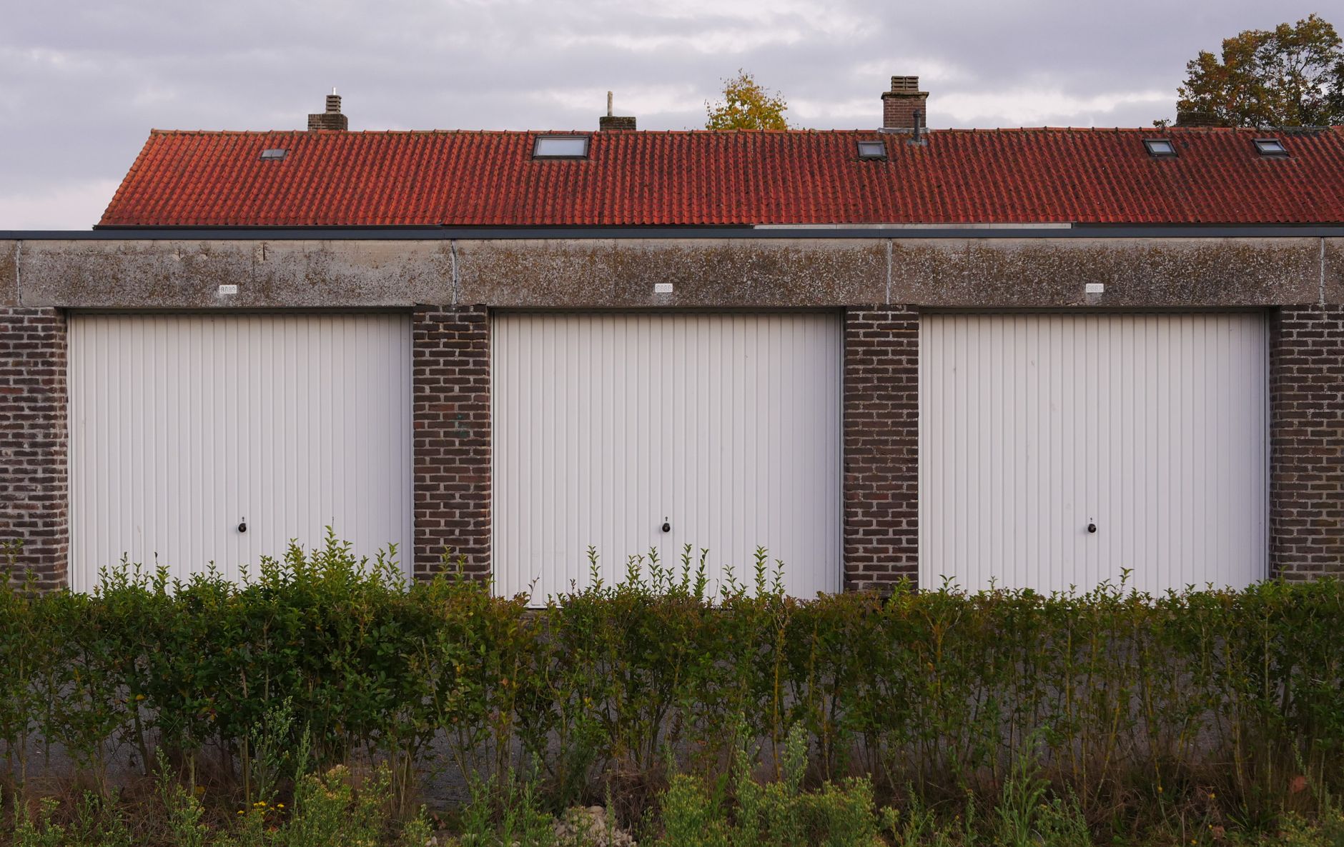 Row of suburban brick garages with red tile roofs under an overcast sky.