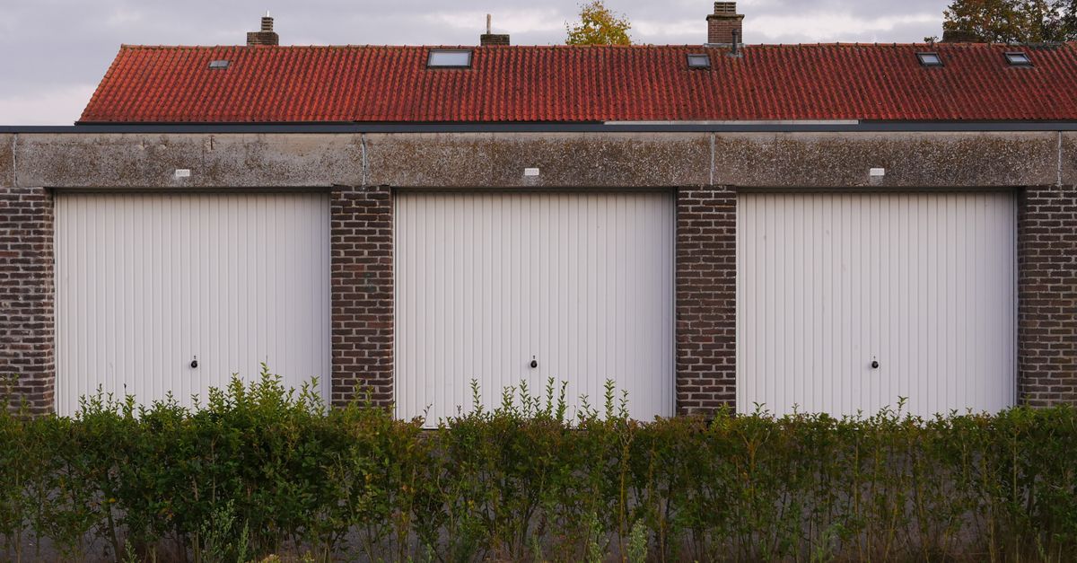 Exterior view of brick garages with red tiled roof and surrounding greenery under a cloudy sky.