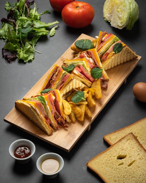 Free Gourmet club sandwich with fresh vegetables and fries on a wooden platter. Stock Photo