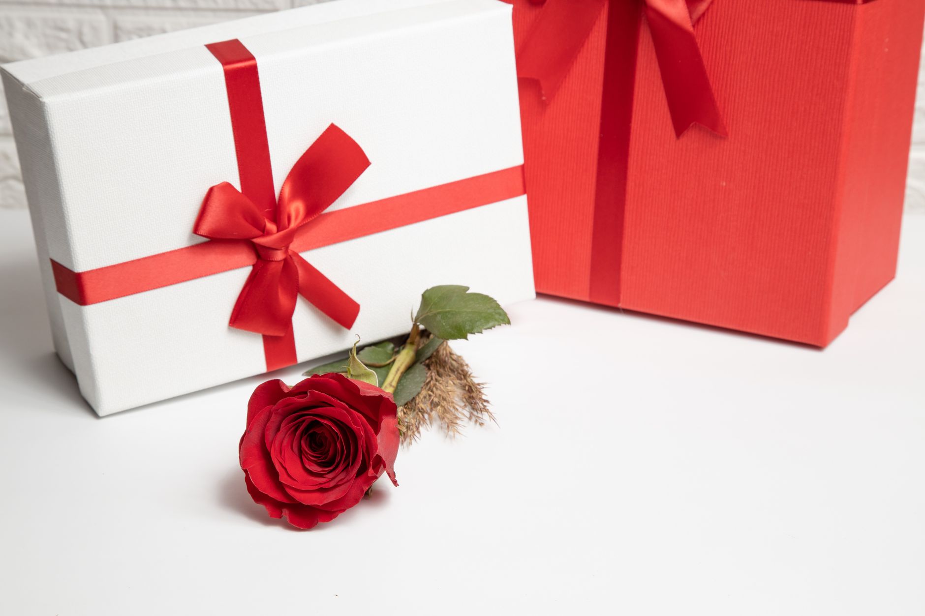 Stylish gift boxes adorned with red ribbons and a delicate red rose for a luxurious presentation.