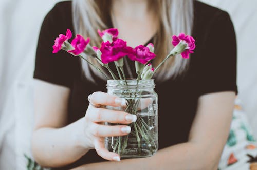 Person Holding Mason Jar With Purple Flowers Inside