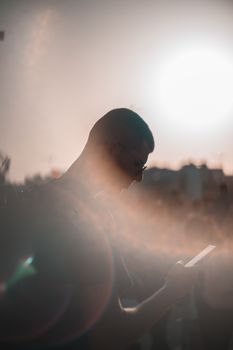 A man in silhouette against a sunlit backdrop, engaged with his phone.