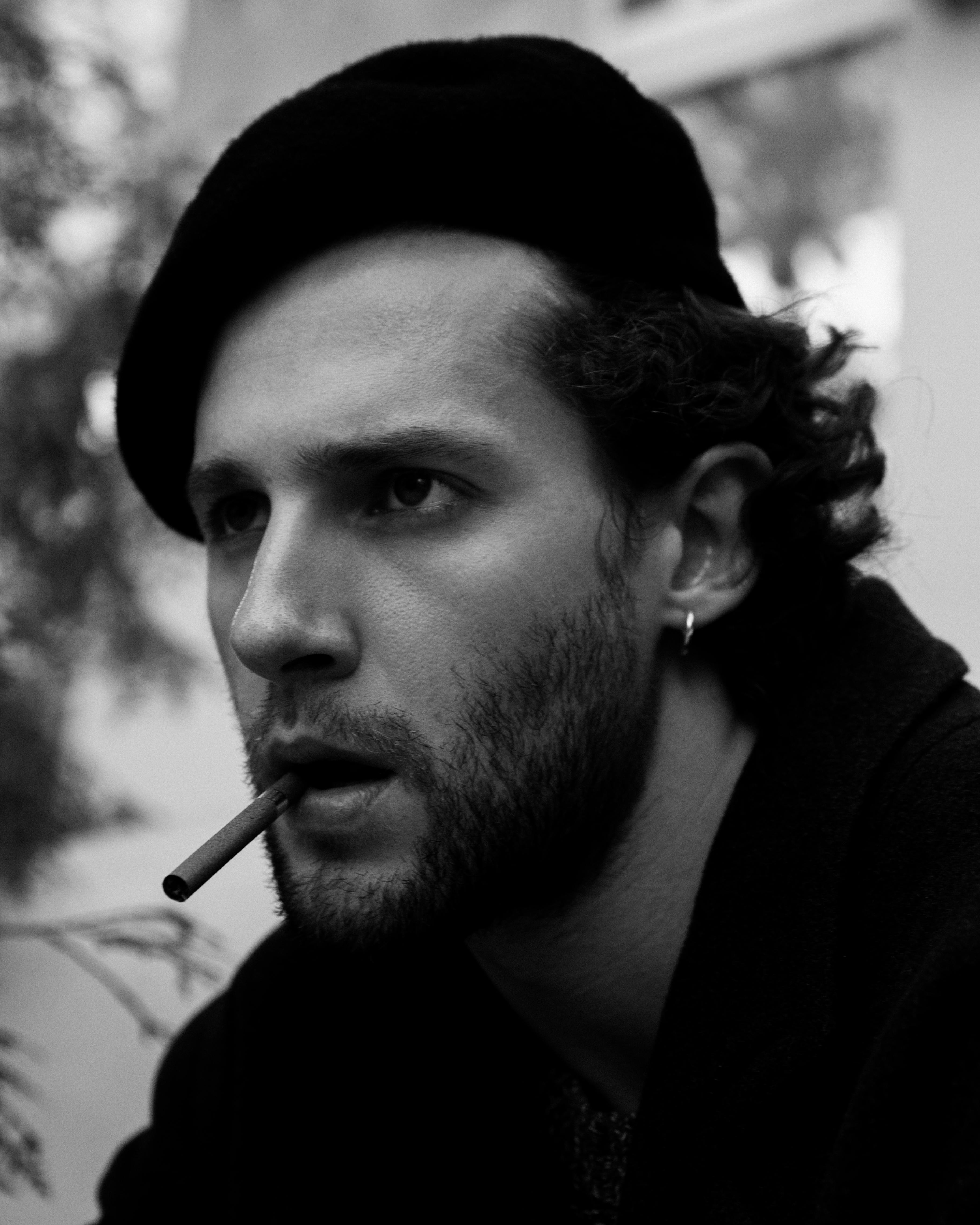 A bearded man in a beret smokes a cigarette in an outdoor setting.