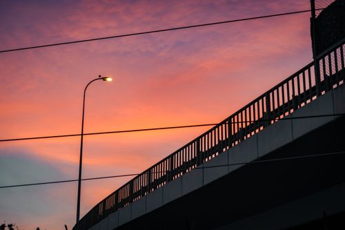 Free A silhouetted bridge and streetlight against a vibrant sunset sky create a striking urban scene. Stock Photo