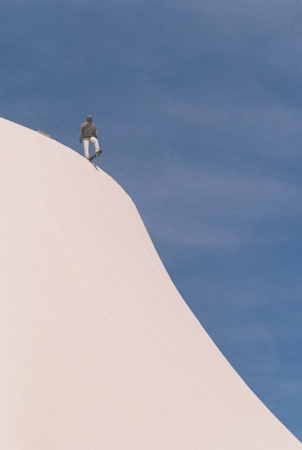 A skateboarder stands atop a white hill with a bright blue sky in Le Havre, France.