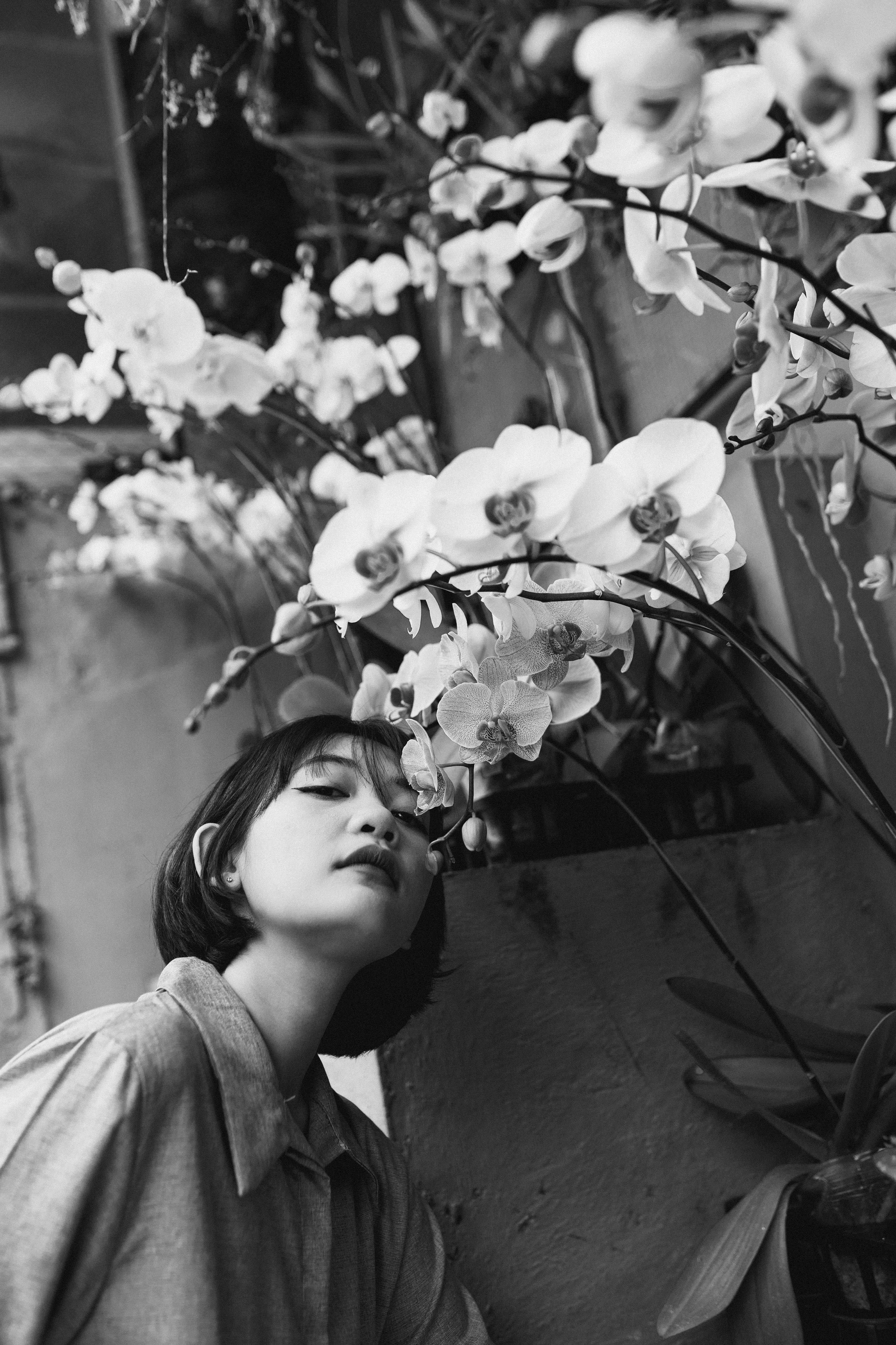 Lively monochrome portrait of an Asian woman smelling orchids indoors.