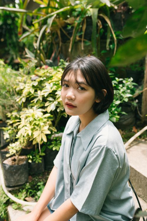 Free Portrait of an Asian woman with short hair, seated in a vibrant garden. Stock Photo